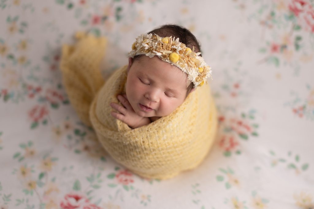 Greater Boston newborn photography portrait of a sleeping baby girl wrapped in yellow with a floral headband.