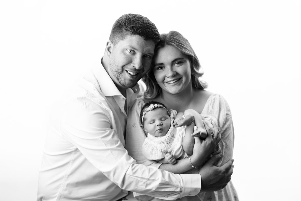 Happy parents holding their sleeping newborn baby girl during a professional Boston newborn photography family portrait session.