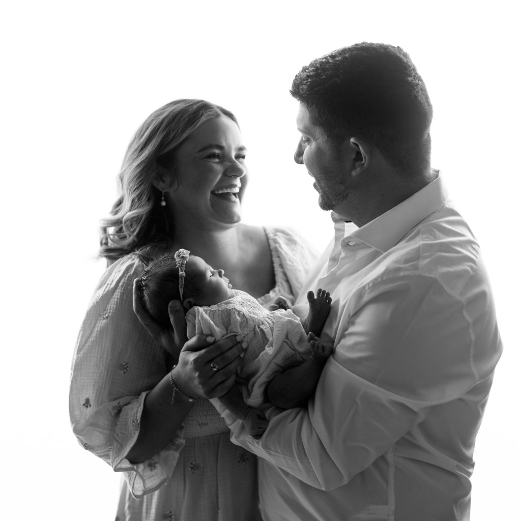 Parents laughing together while holding their newborn daughter during a Boston family newborn photography session.