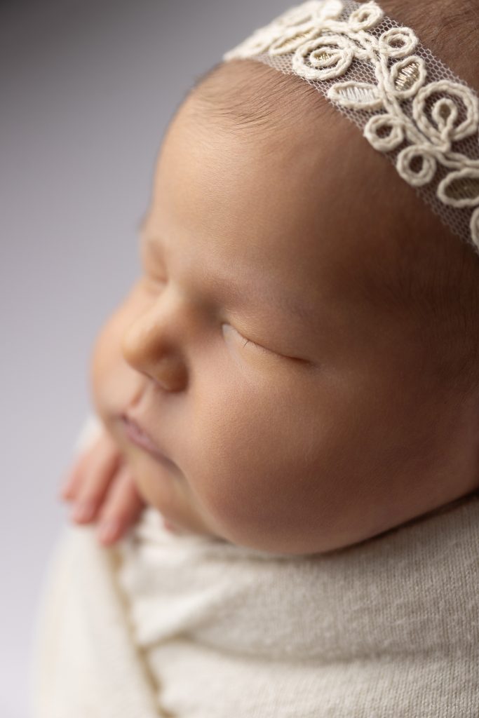 Close-up of a sleeping newborn wearing a delicate headband during a professional studio newborn photography session in Norwood, Massachusetts.
