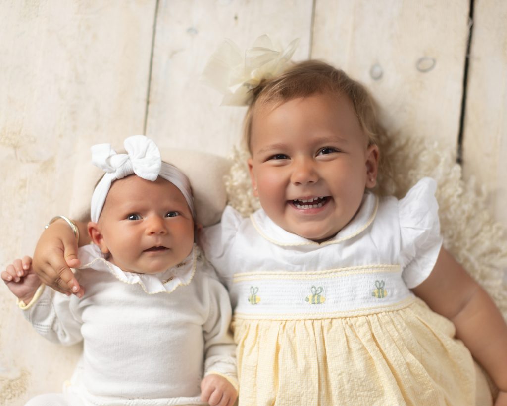 Smiling older sister cuddling her newborn sibling during a professional studio newborn photo session in Norwood, MA.