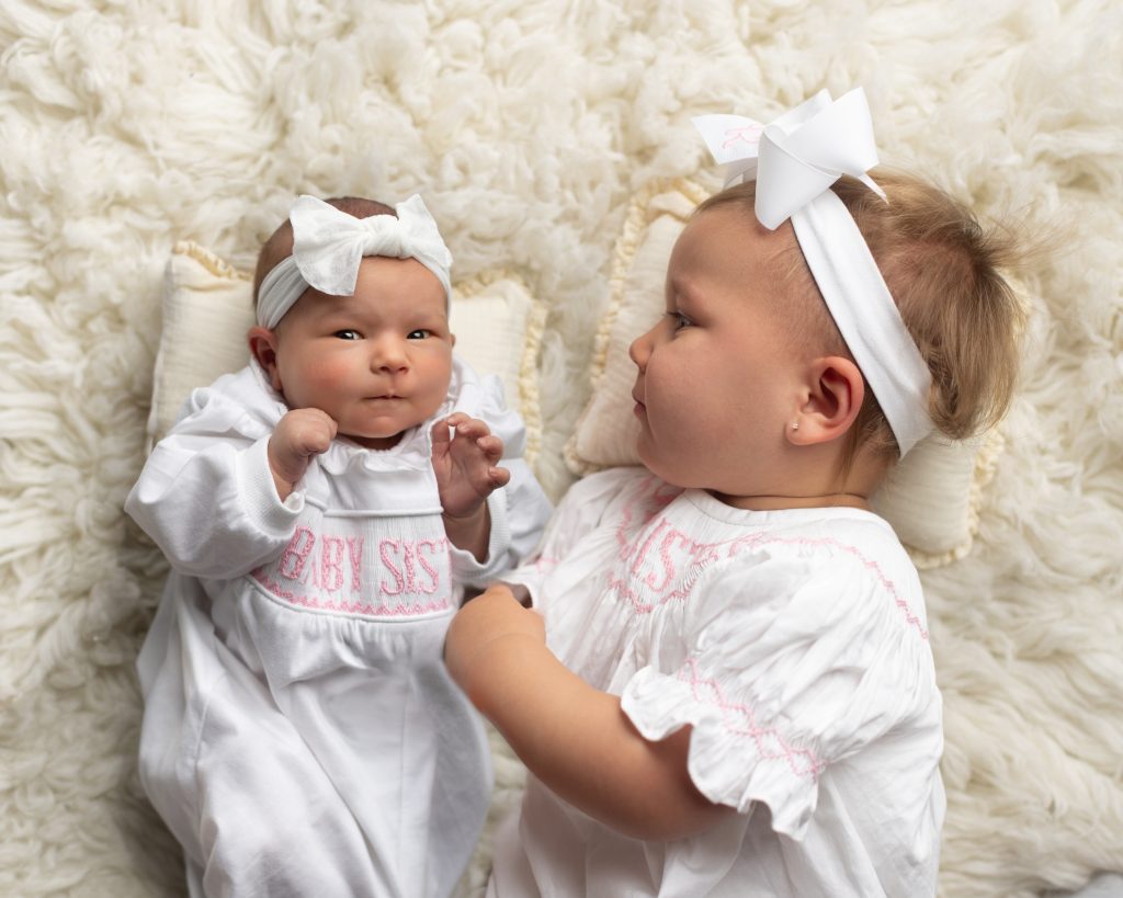 Older sister gazing lovingly at her newborn baby sister during a studio newborn photography session.