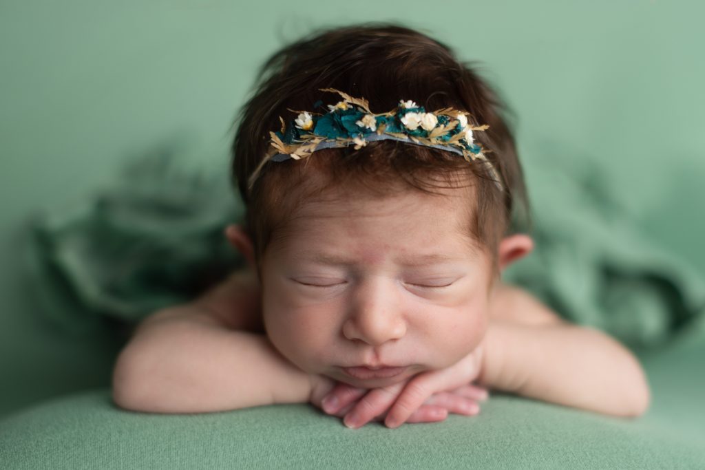 Sleeping newborn baby posed on a soft green blanket with a delicate floral headband