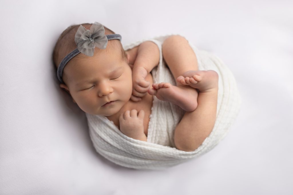 Sleeping newborn posed naturally on a soft white backdrop during a professional newborn studio session in Greater Boston.