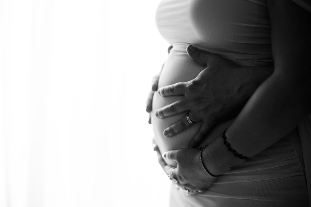 Close-up maternity photograph of parents' hands gently holding a pregnant belly.