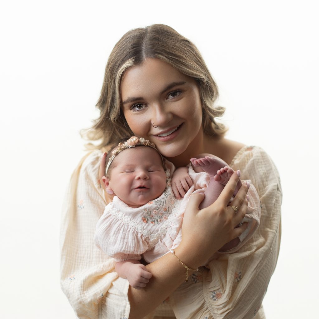 Mother holding her smiling newborn baby girl during a professional newborn photography session near Boston.