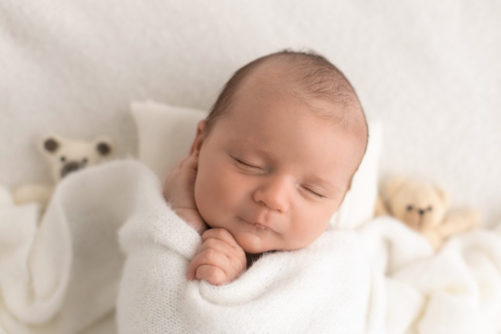 Sleeping newborn wrapped in white with small teddy bears in the background