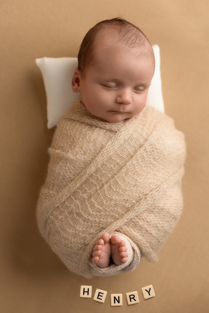 Newborn baby swaddled in beige with wooden letters spelling Henry