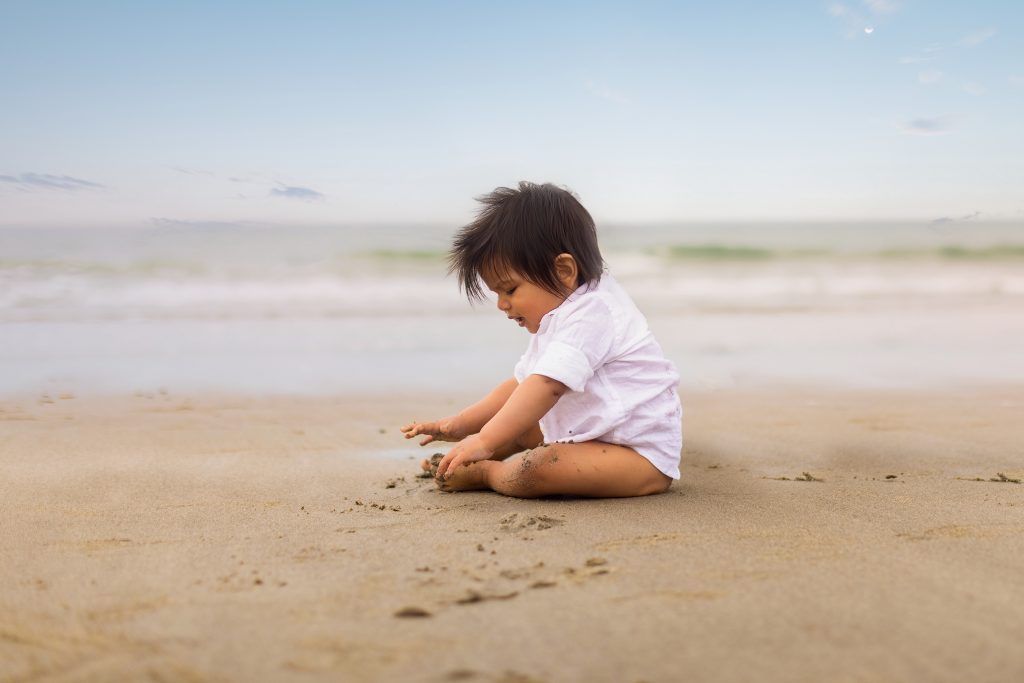 6-month-old baby boy sitting and playing in the sand during a beach photo session in Gloucester, Massachusetts