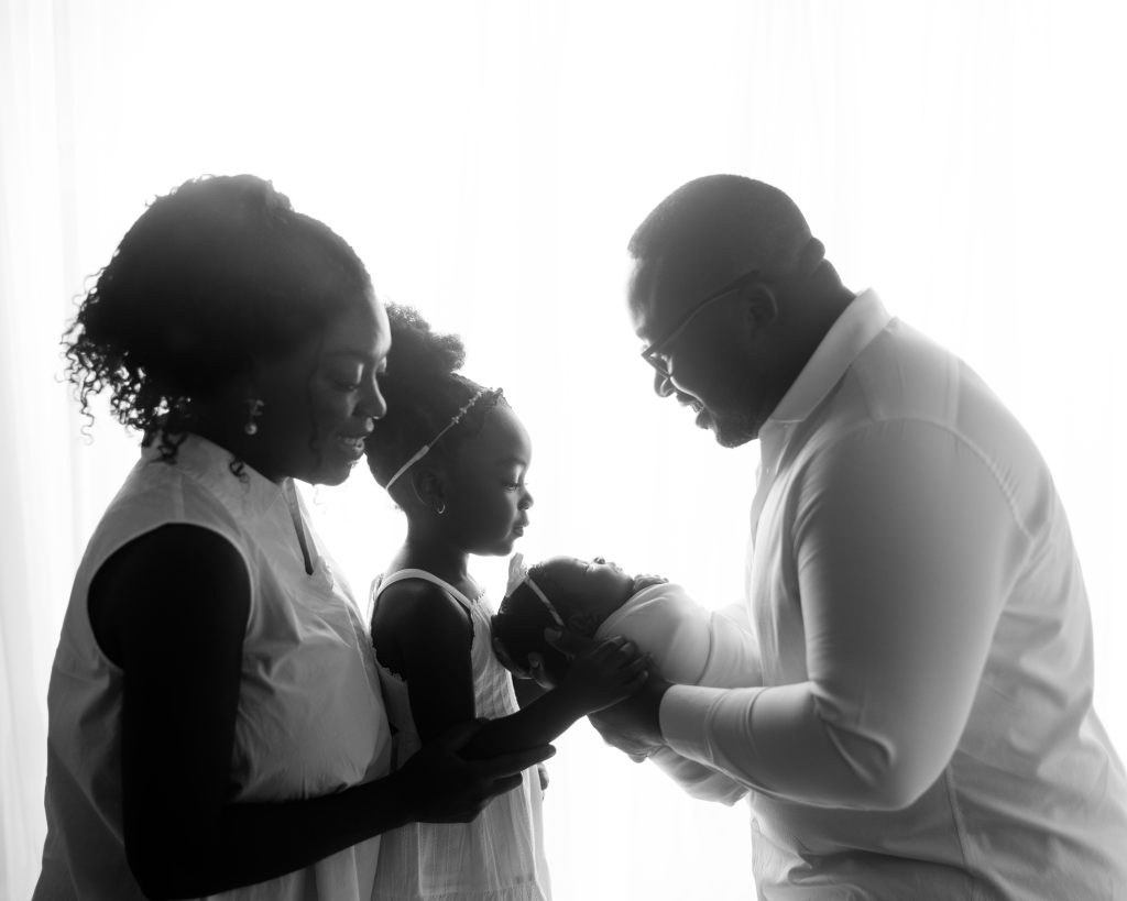 Parents and older child gathered around a swaddled newborn baby for a family portrait