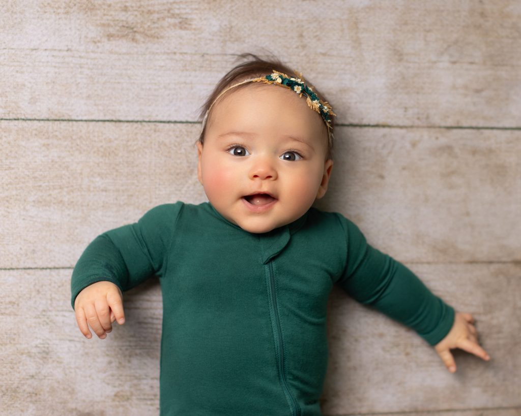Smiling baby in a green outfit and floral headband during a studio milestone portrait session.