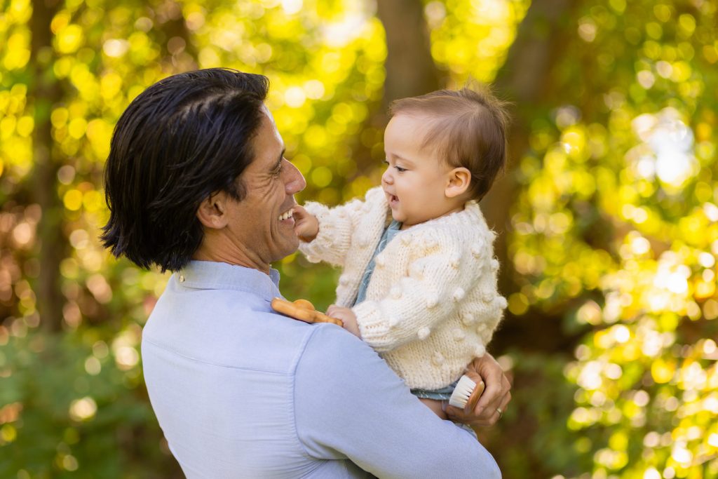 Parent holding a laughing baby outdoors during a first-year milestone photography session.
