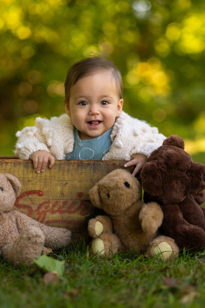 Smiling baby outdoors with vintage teddy bears during a milestone photography session.