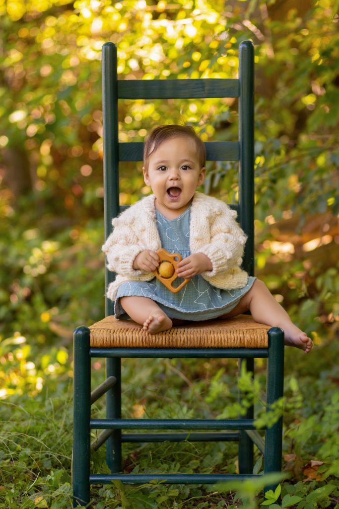 Happy baby sitting independently on a chair outdoors during a first-year milestone photo session.