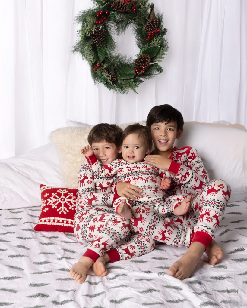 Three siblings in matching holiday pajamas during a first-year baby photography session near Boston.