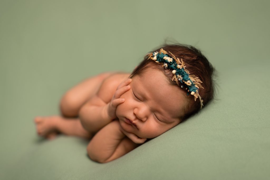 Sleeping newborn wearing a delicate floral headband on a soft green backdrop.