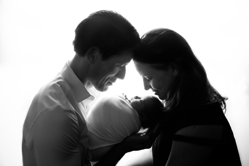 Black-and-white portrait of two parents holding their newborn baby during a newborn photography session.